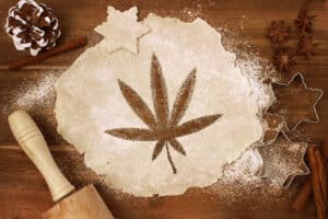 Wooden table with rolling pin and cookie dough with marijuana leaf cut out