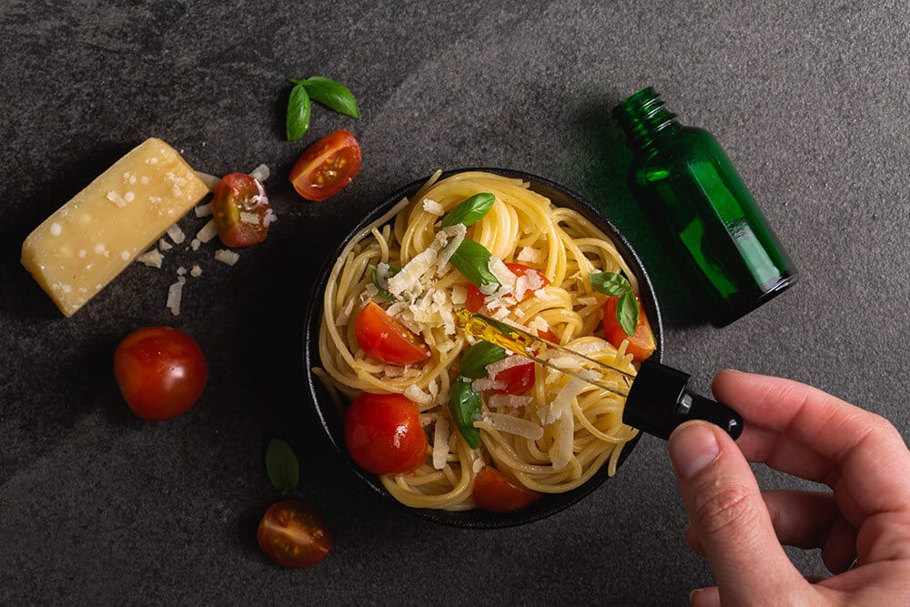 Hand adding drops from tincture to pasta