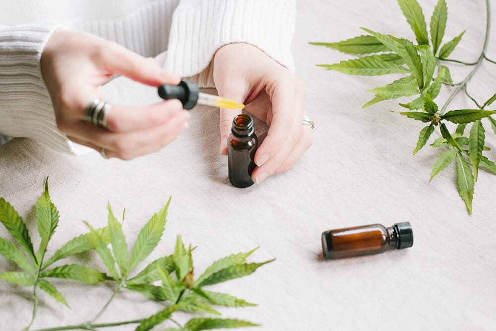 Womans hands holding tincture with marijuana leafs around