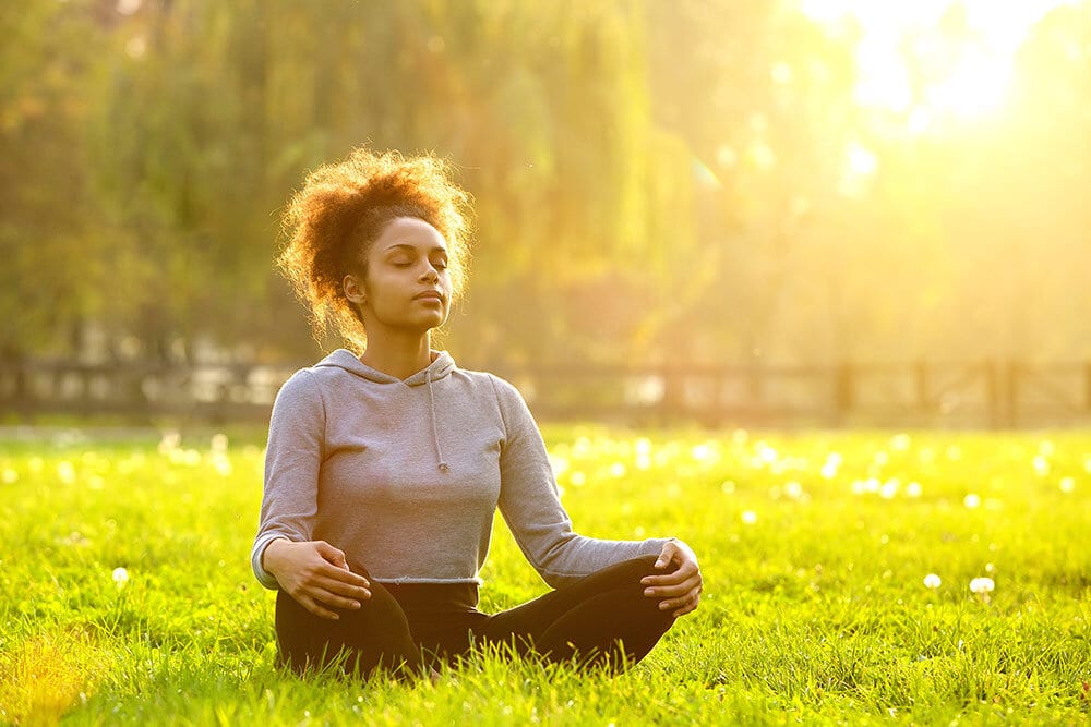 Young woman meditating in grass in outside open area