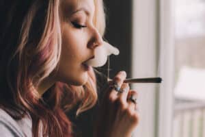 Young woman smoking marijuana joint by window
