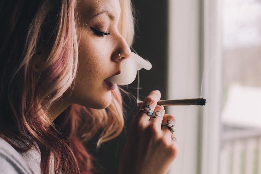 Young woman smoking marijuana joint by window