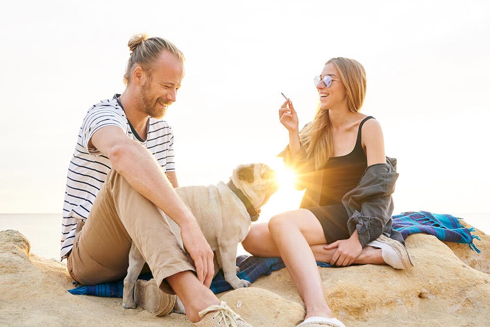 Couple sitting at the beach with their dog smoking weed and having fun