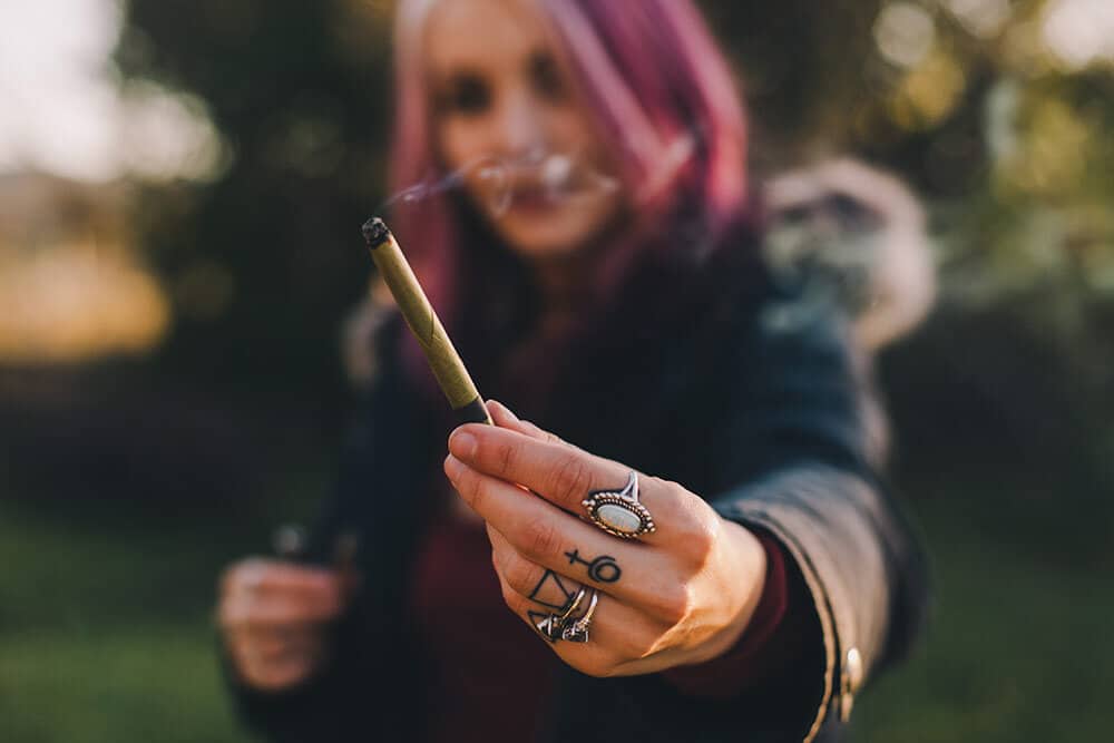 Woman holding out cannabis joint outside