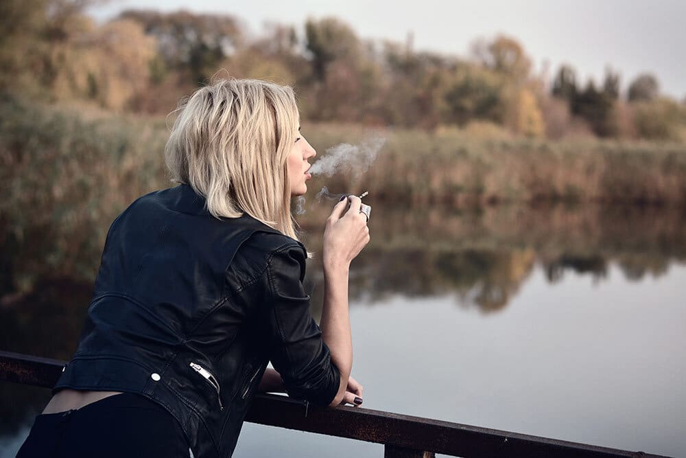Woman standing on deck near water smoking marijuana