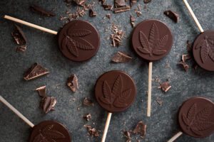 Chocolate cannabis lollipops laid out on table with chocolate pieces around