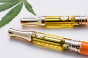 Cannabis plant leaf next to vape pens with cannabis extract