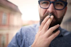 Man walking outside in glasses smoking cannabis blunt