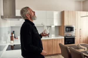 Older man standing in kitchen smoking cannabis flower with bong