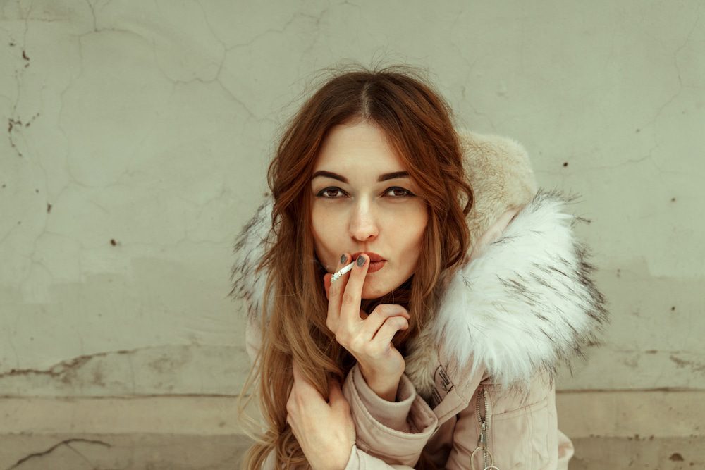 A young woman in a winter coat smoking cannabis outdoors