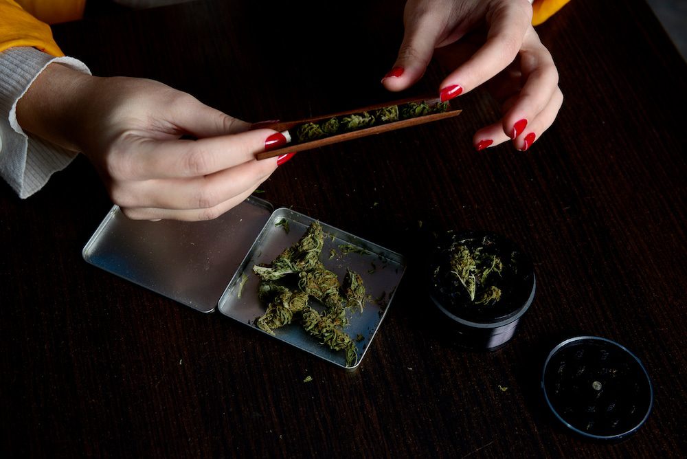 A young woman rolls up her weed into a joint